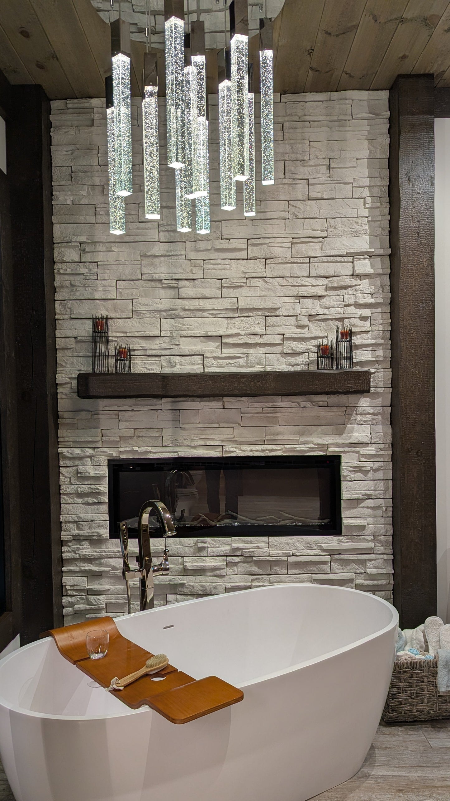 Modern bathroom with freestanding bathtub, timber mantel, decorative timber posts, stone fireplace, and decorative lighting.